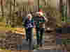 Two teenagers running in the woods wearing Santa hats 